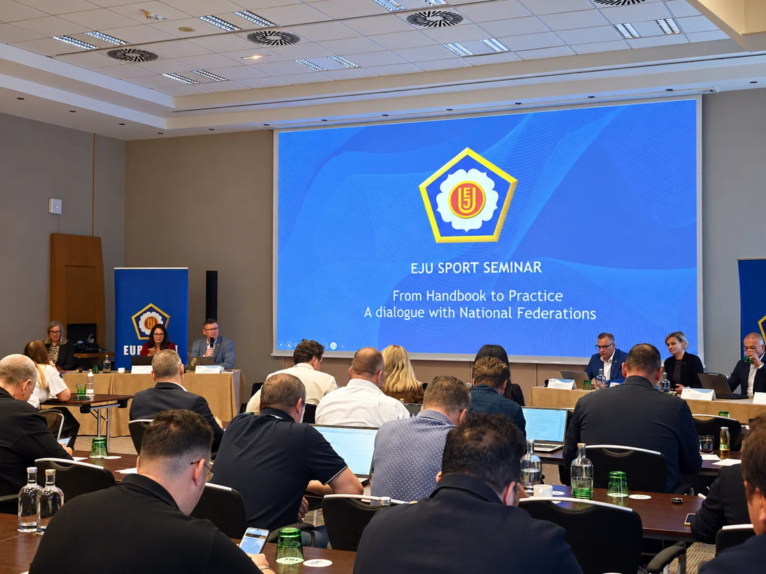 Attendees sit at tables facing a presentation screen during an EJU Sport Seminar, with speakers seated at the front.